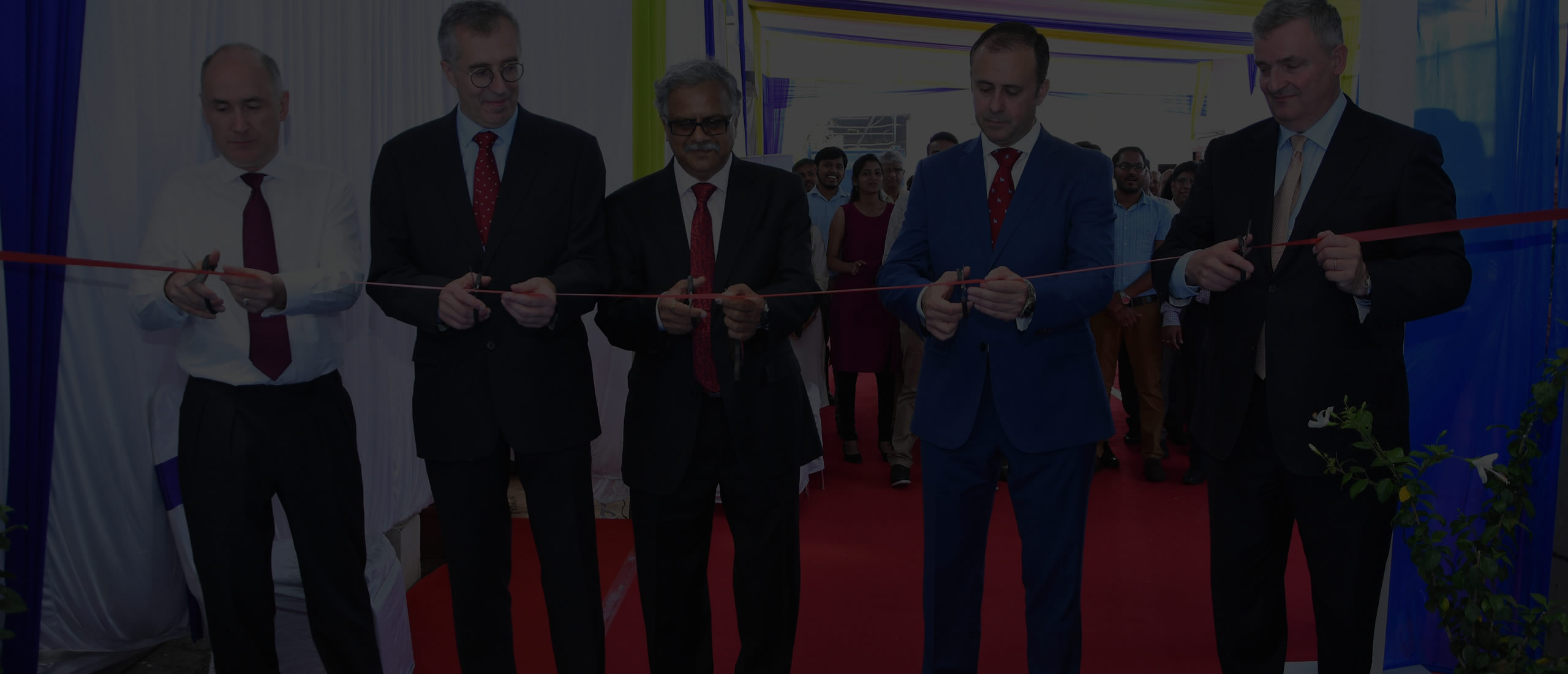 5 men cutting red ribbon