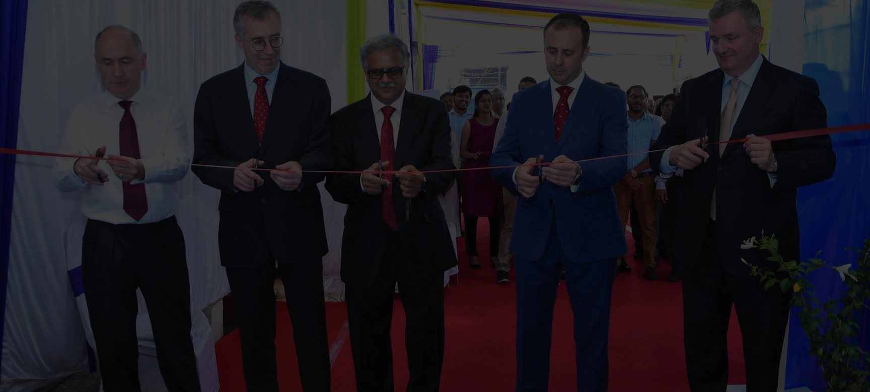 5 men cutting red ribbon
